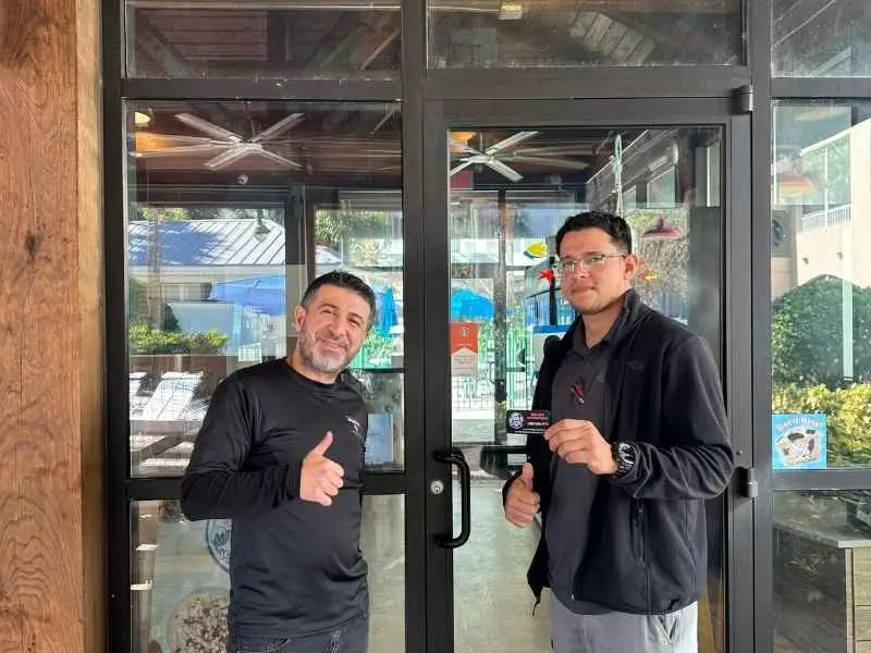 Two professional locksmiths standing in front of a secured commercial glass door, giving a thumbs-up after completing a commercial locksmith service in Sanford.