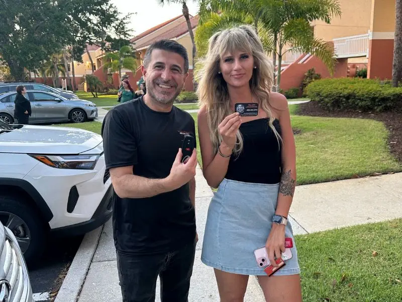 A satisfied customer holding a locksmith service card next to a professional locksmith in Sanford, after receiving car key replacement or locksmith assistance.